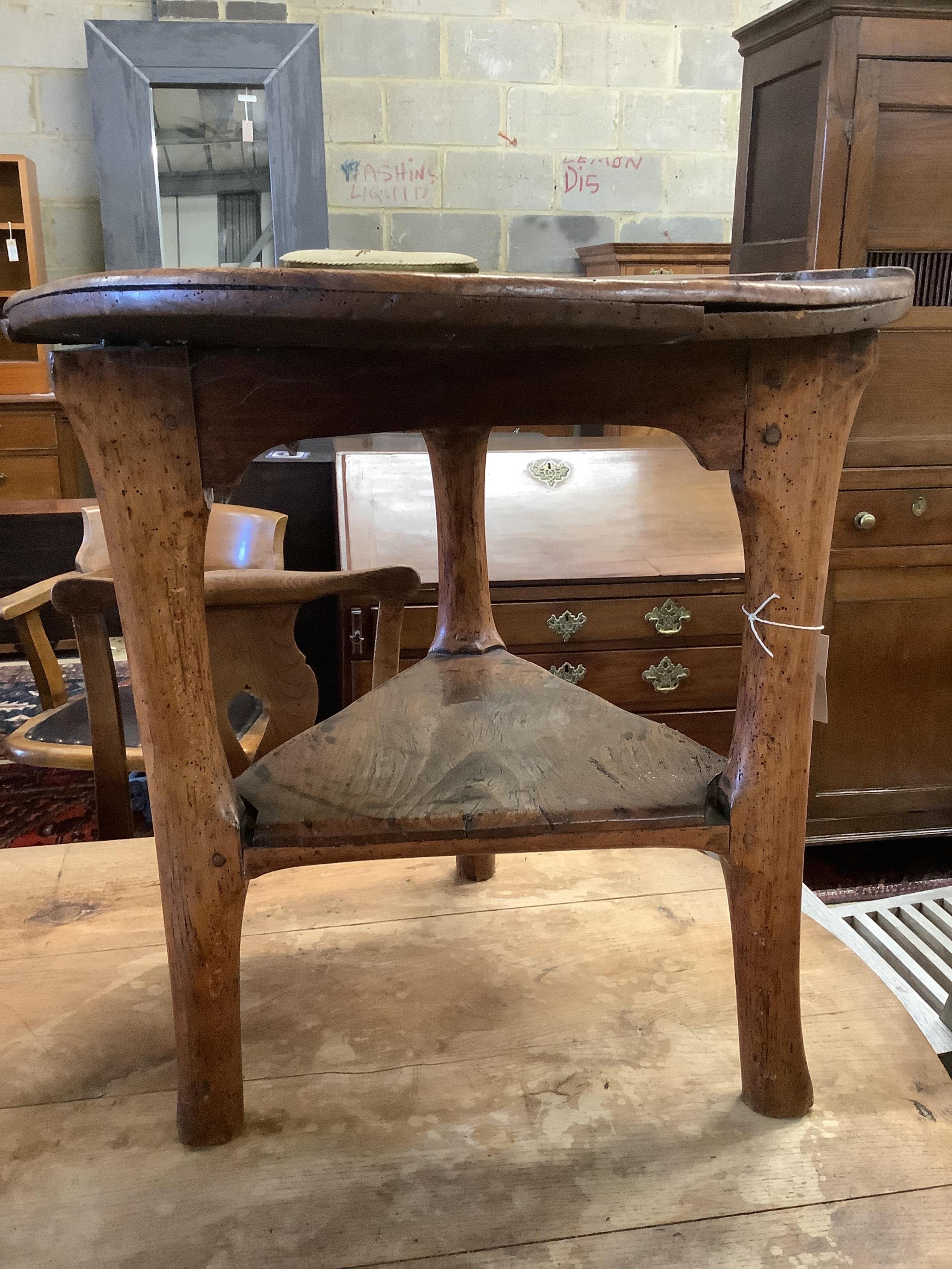 An 18th century elm cricket table, width 63cm, height 64cm. Condition - extensive splitting and old patches and repairs to the top, legs probably reduced, but full of character